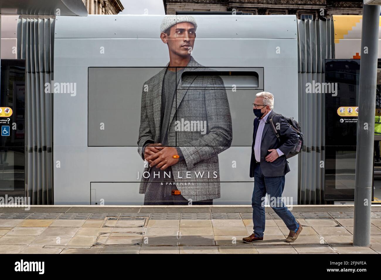 Mann mit Gesichtsmaske, der an einem Werbespot von John Lewis auf der Seite einer Straßenbahn in Edinburgh vorbei läuft. Stockfoto