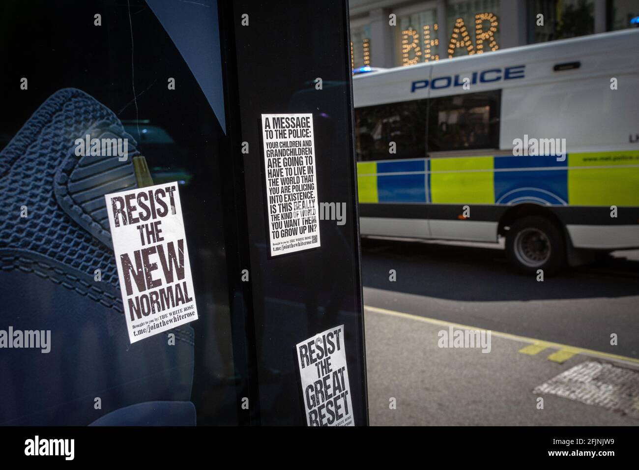 24. April 2021, London, England, Vereinigtes Königreich: Bushaltestelle mit Aufklebern und Polizeiwagen, der während eines Anti-Lockdown-Protests in London vorbeifährt. Stockfoto