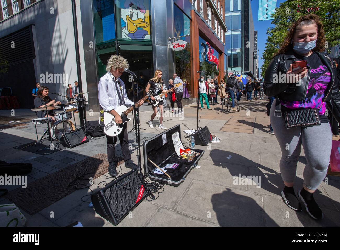 Menschen mit schützenden Gesichtsmasken passieren Live-Bands, die während der Coronavirus-Pandemie in der Oxford Street in London spielen. Stockfoto