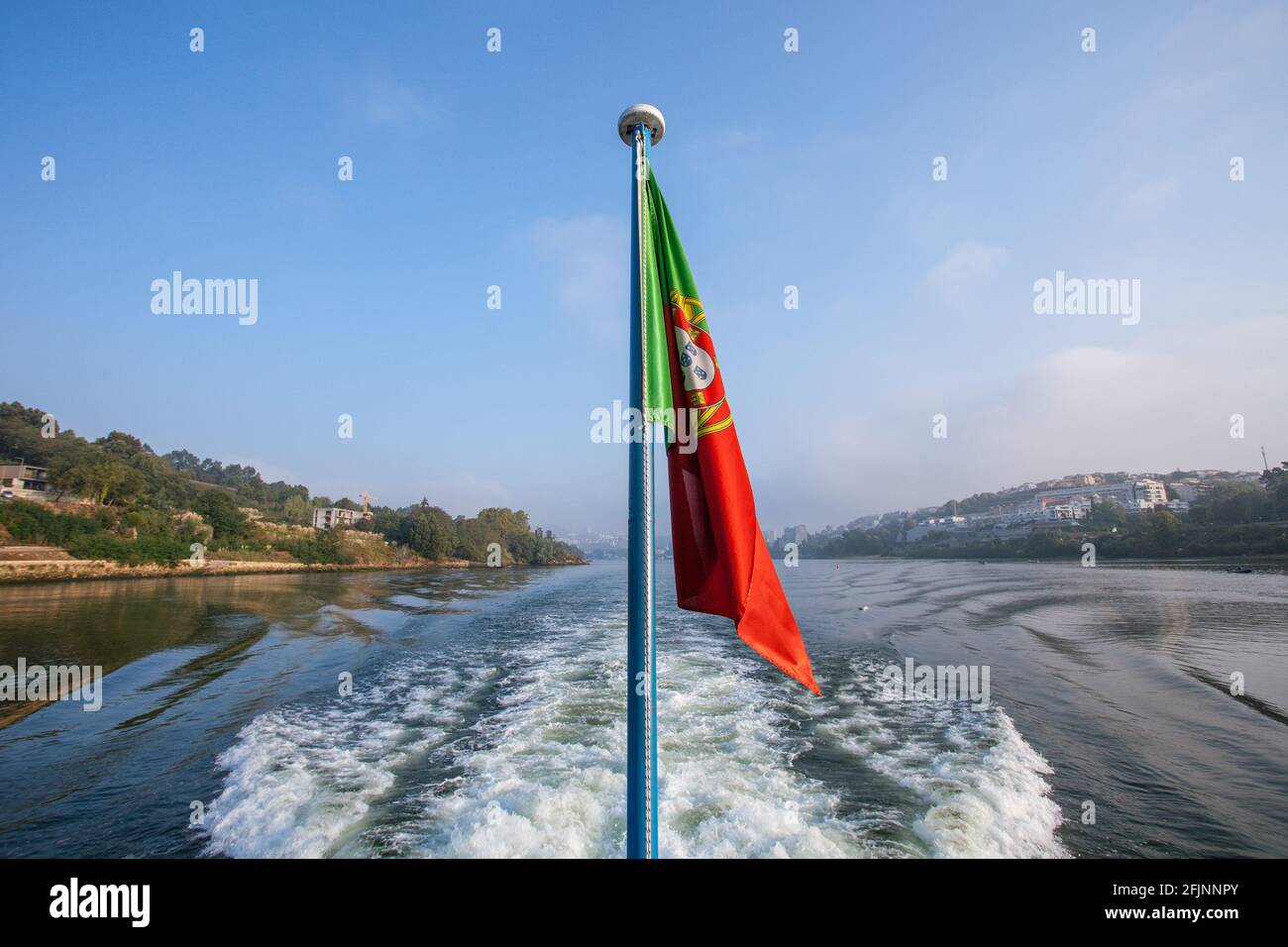 Die portugiesische Flagge, die auf dem hinteren Teil eines Kreuzfahrtschiffes im Douro-Tal im Norden Portugals schwimmt. Stockfoto