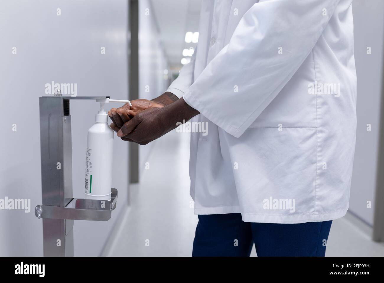 Mittelteil des afroamerikanischen männlichen Arztes in weißem Fell desinfizieren Hände im Krankenhausflur Stockfoto