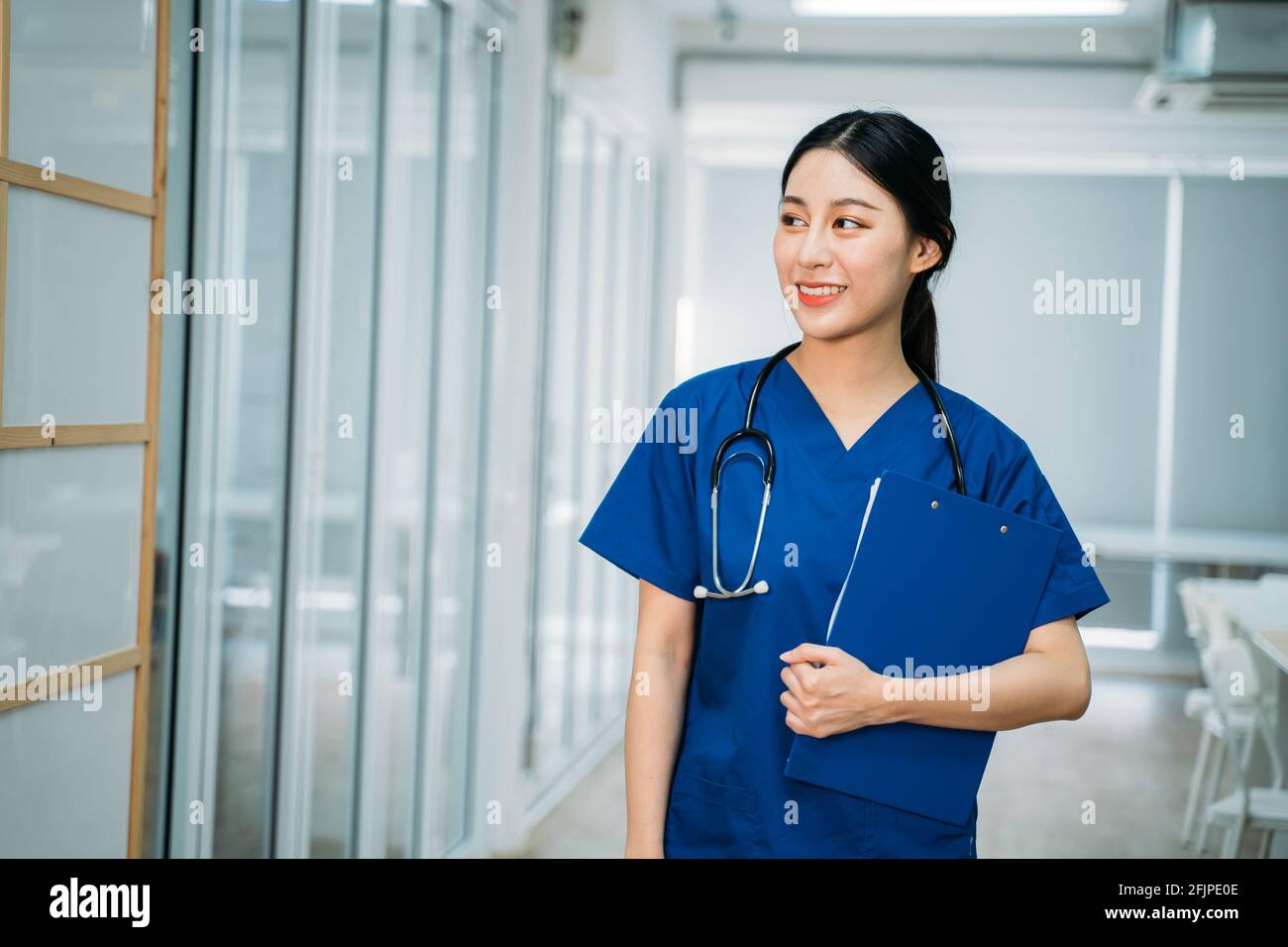 Junge schöne asiatische Ärztin in Uniform mit Stethoskop stehend Im Krankenhausflur hält man die Zwischenablage und überprüft Berichte, während man wegschaut Stockfoto