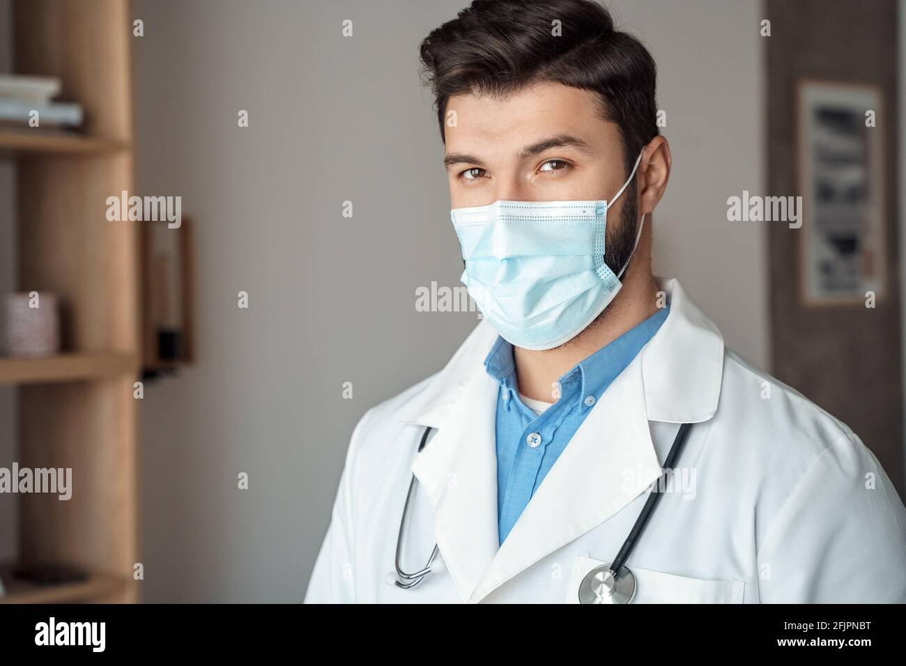Kaukasischen jungen Arzt im Gesicht Maske weißen medizinischen Mantel mit Stethoskop, Hochformat Stockfoto