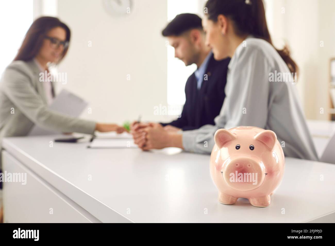 Sparschwein auf Kreditmakler Schreibtisch aus der Nähe, Paar unterzeichnet Vertrag im Hintergrund Stockfoto
