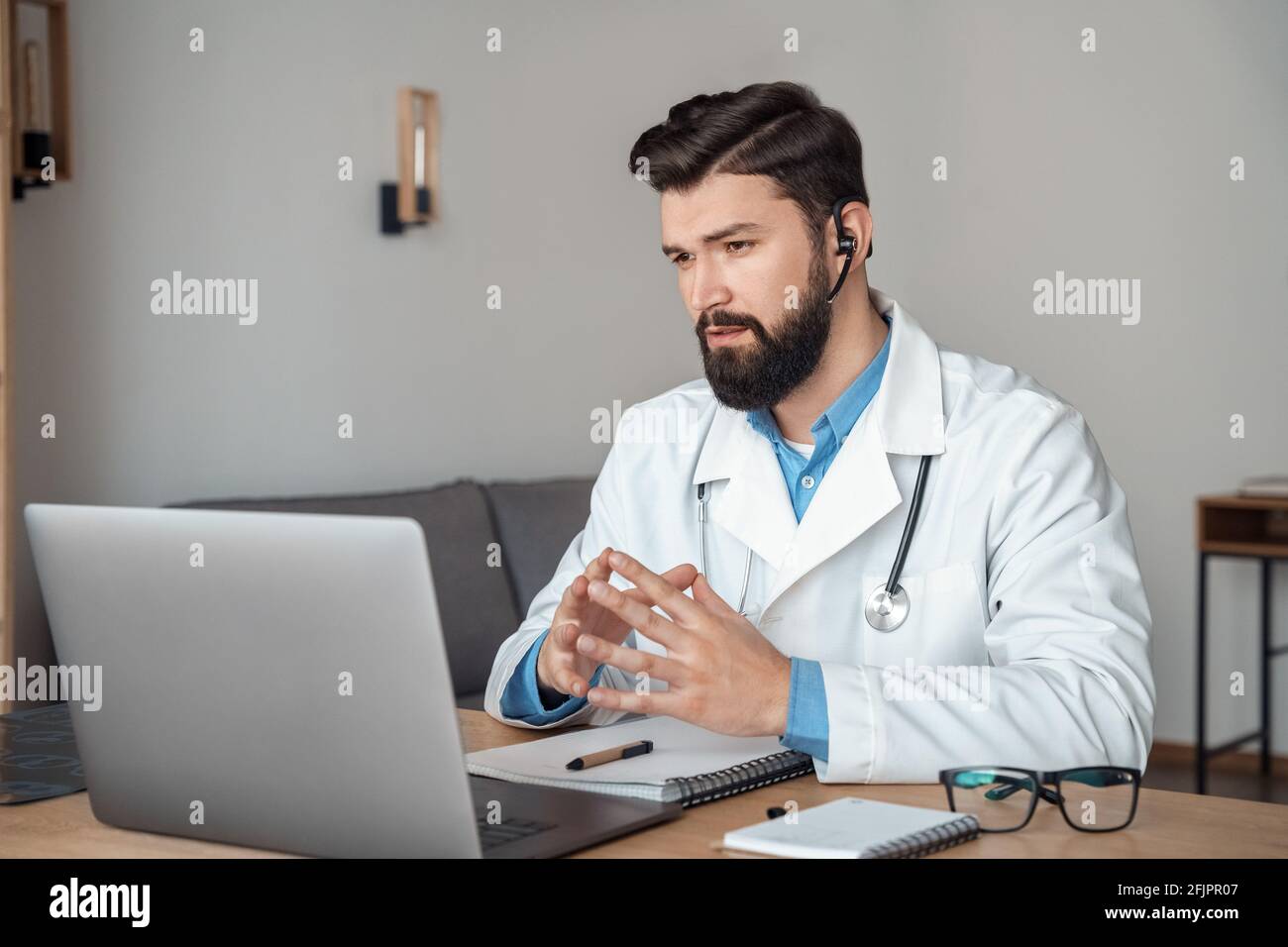 Kaukasischer Mann Arzt in drahtlosen Kopfhörern, die Patienten Remote online beraten Stockfoto