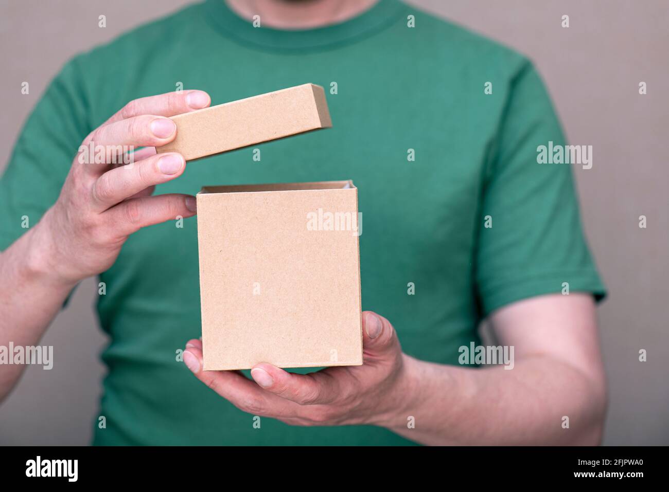Ein Mann, der in einem grünen T-Shirt gekleidet ist und kleine Pappkartons hält Box mit offener Kappe Stockfoto