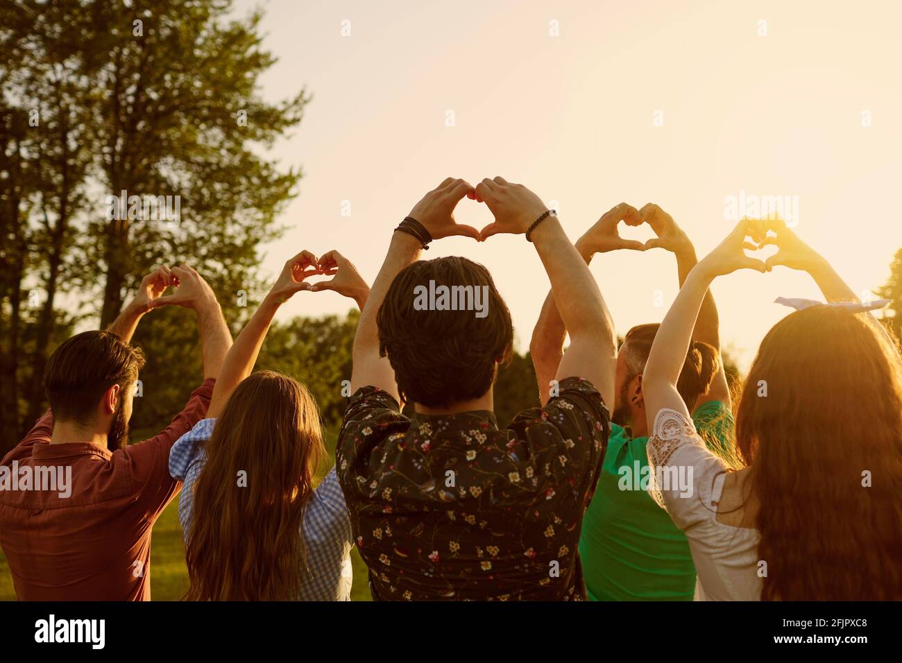 Hand Zeichen Herz. Eine Gruppe von Menschen hält Hände mit einem Herzzeichen auf einem Himmel Hintergrund mit Sonnenuntergang auf der Natur. Stockfoto