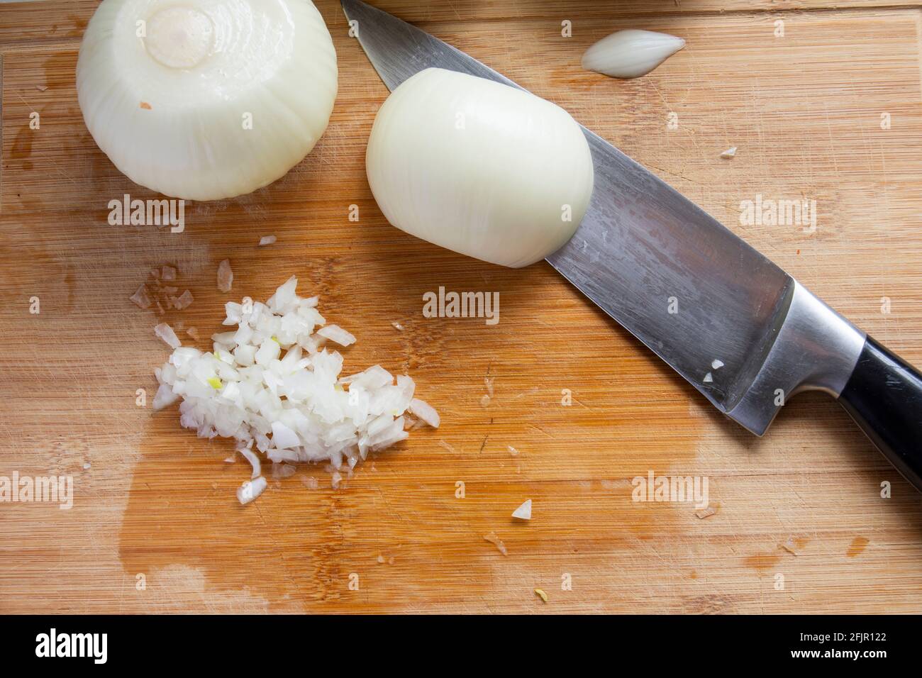 Während der Zubereitung von Hamburgern werden weiße Zwiebeln mit einem Kochmesser gehackt. Selektive Zwiebeln fokussieren. Draufsicht. Stockfoto