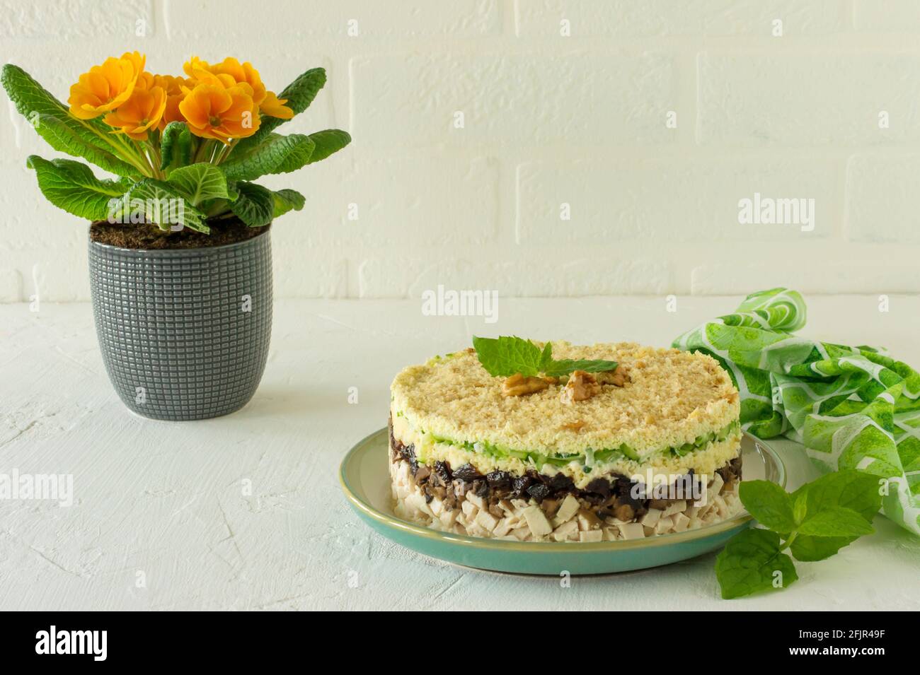 Geschichteter Salat mit Huhn, Pilzen, Pflaumen, Eiern, Gurken und Käse auf einem Teller auf weißem Grund serviert, Stockfoto