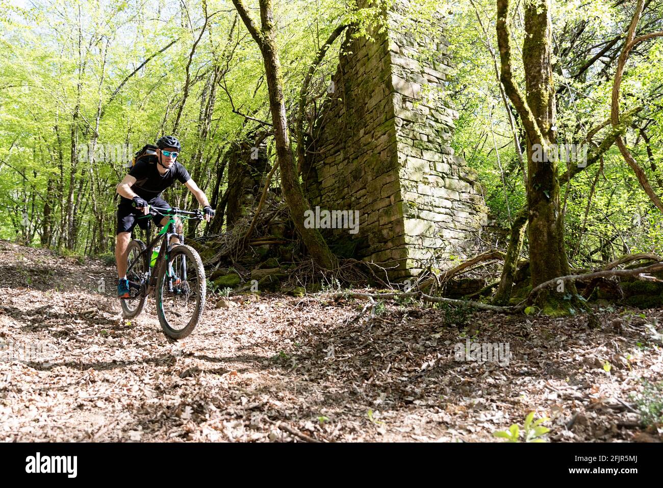 Der Mensch fährt mit dem Dirtbike in der Frühlingslandschaft bergab an einem ruinierten traditionellen Haus, dem slowenischen Haus, vorbei Stockfoto