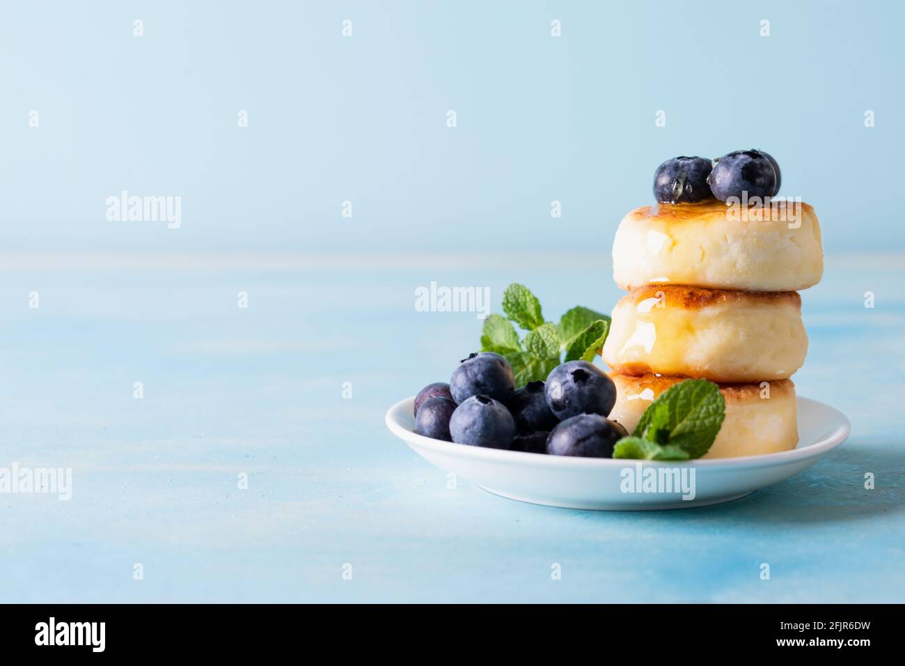 Hüttenkäse-Pfannkuchen. Käsekuchen aus Hüttenkäse, leckeres Frühstück, traditionelle russische süße Pfannkuchen. Mit Heidelbeere, Minze und Honig. Stockfoto