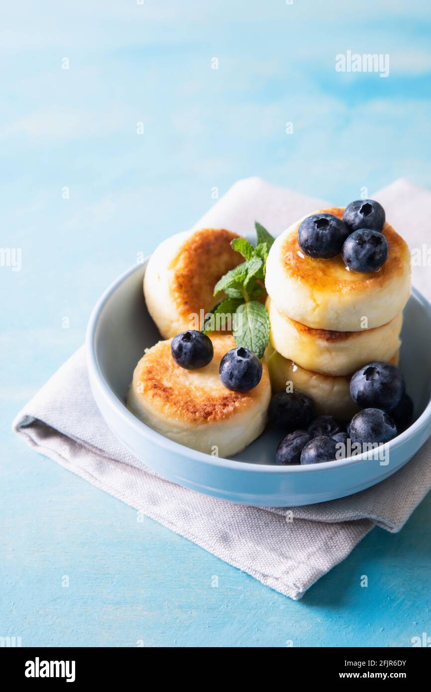 Hüttenkäse-Pfannkuchen. Käsekuchen aus Hüttenkäse, leckeres Frühstück, traditionelle russische süße Pfannkuchen. Mit Heidelbeere, Minze und Honig. Stockfoto