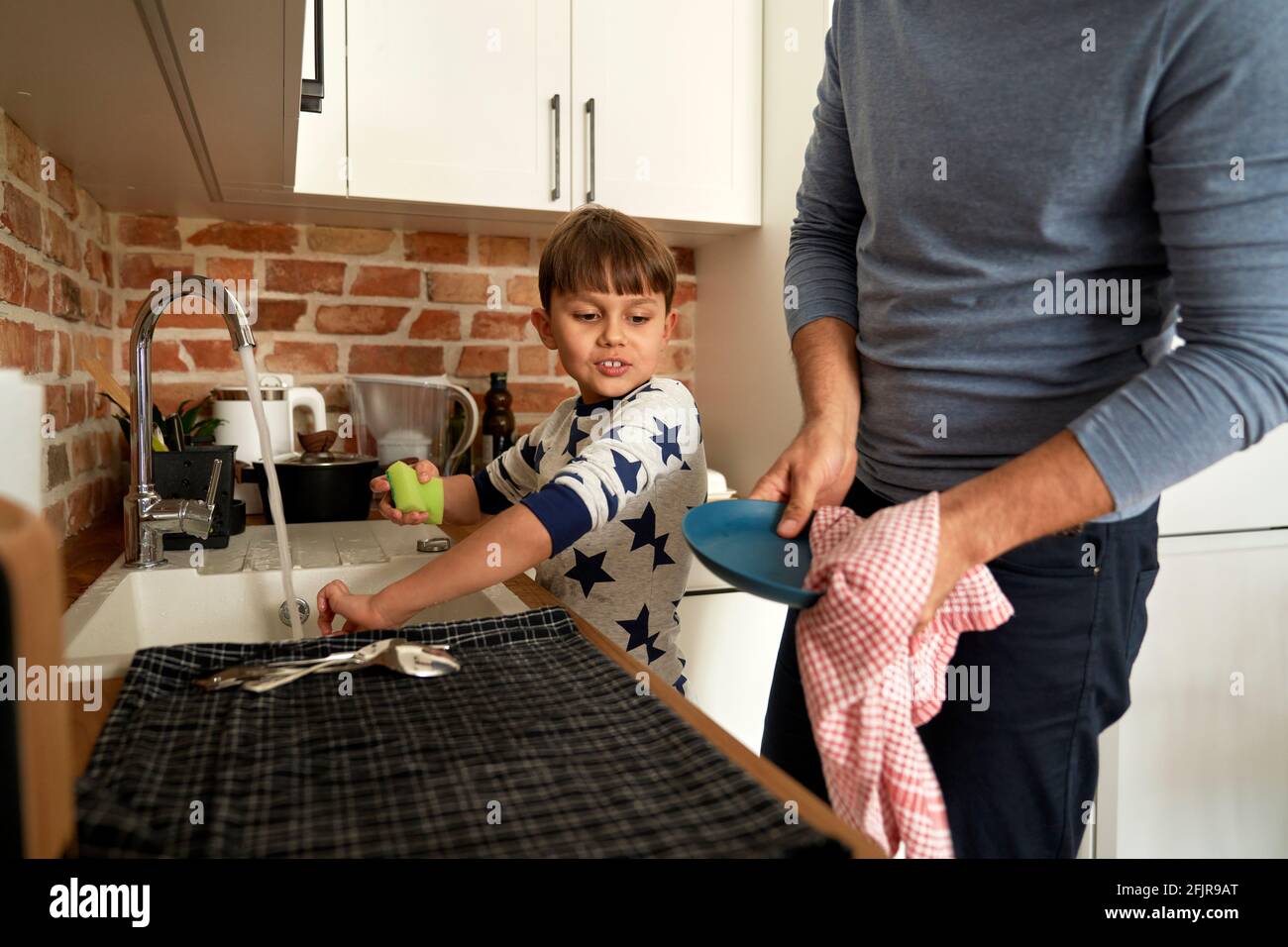 Sohn hilft seinem Vater, das Geschirr zu waschen Stockfoto