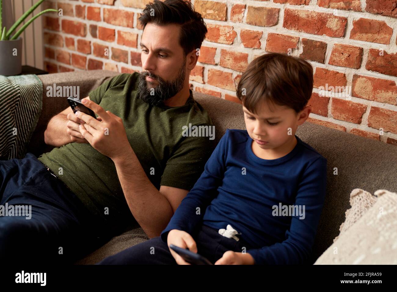 Vater und Sohn sitzen zu Hause mit dem Handy Stockfoto