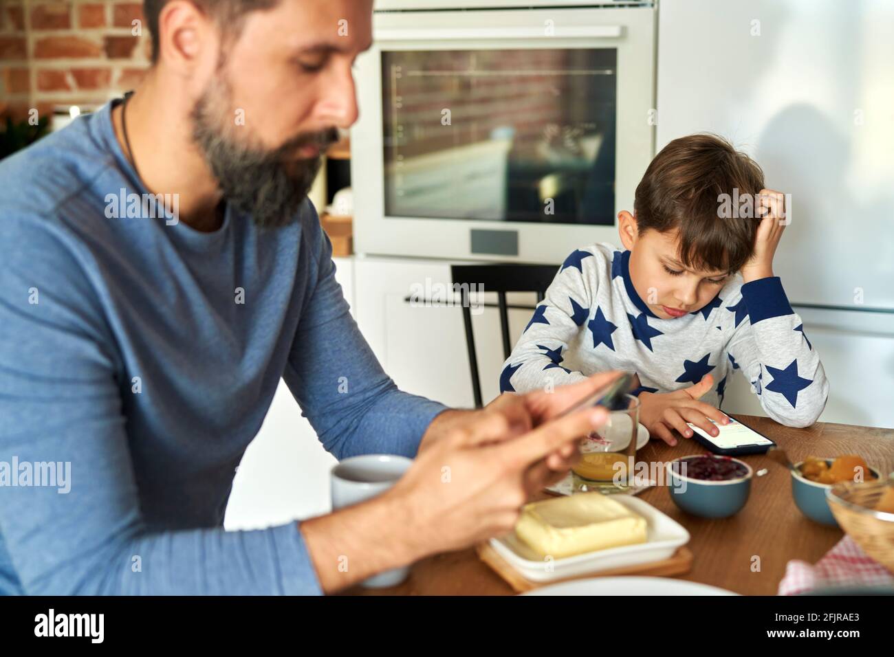 Vater und Sohn sitzen beim Frühstück mit dem Handy Stockfoto