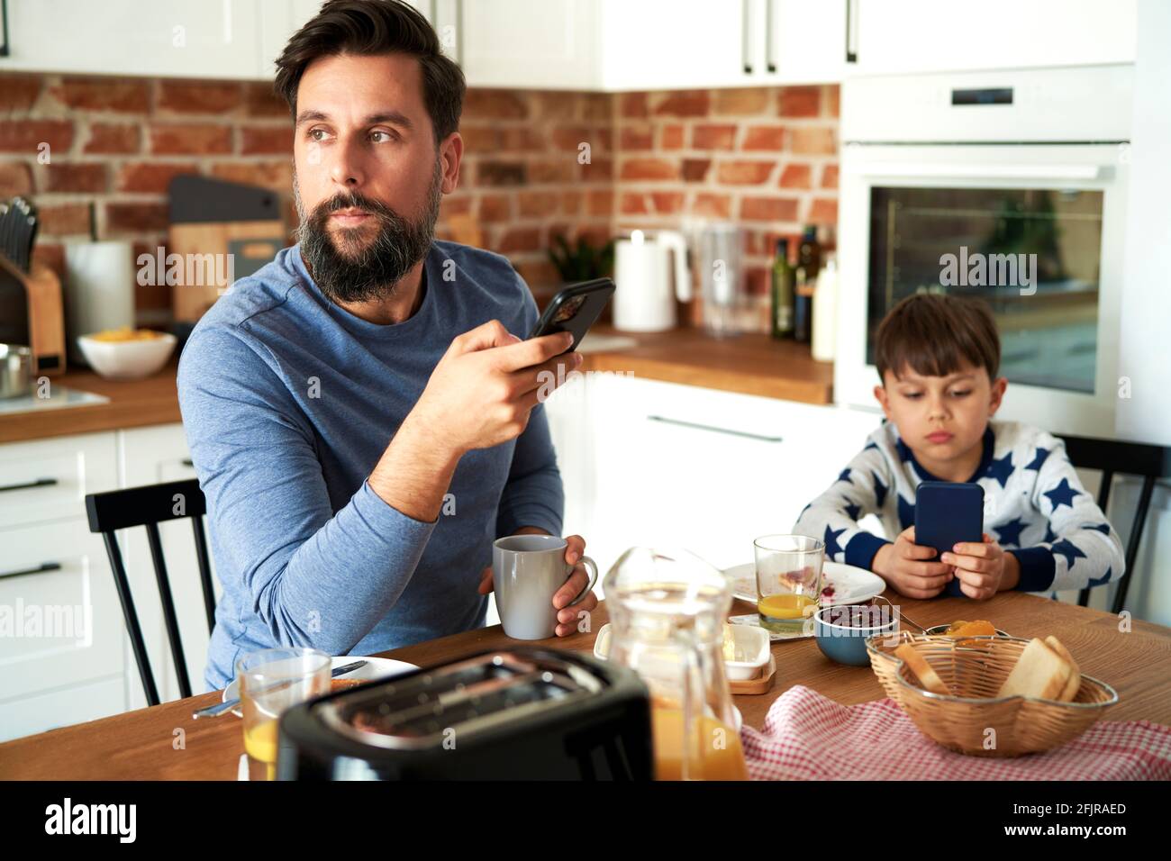 Vater und Sohn beim Frühstück über ein Mobiltelefon Stockfoto