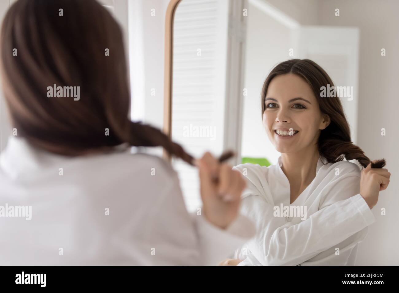 Glückliche junge Frau im Bademantel zieht Büschel der Haare Stockfoto