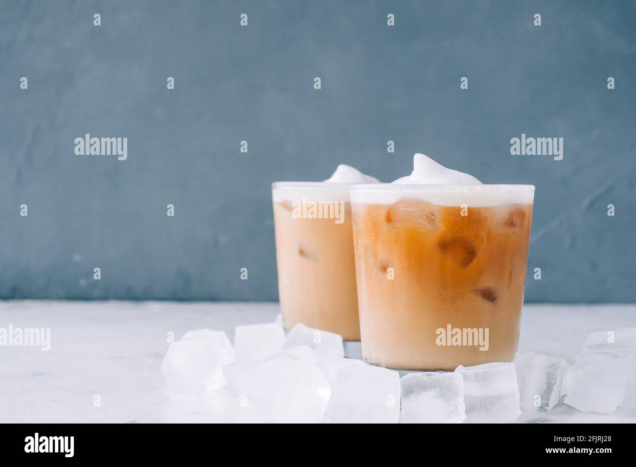 Eisgebrühter Kaffee im Glas mit Milchschaum und Eiswürfeln auf weißem Tisch, Platz kopieren... Stockfoto