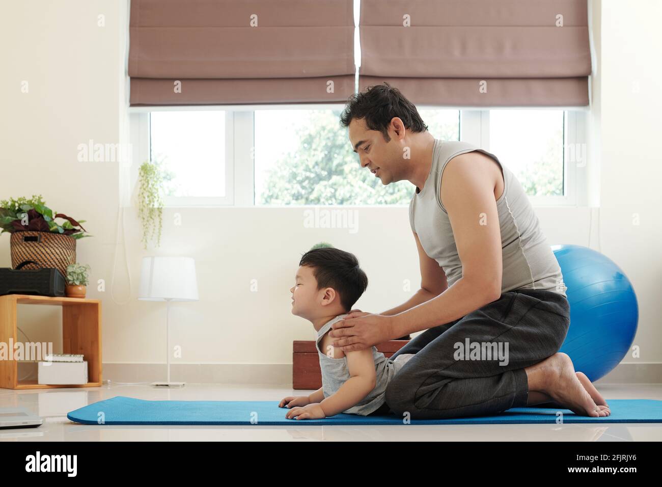 Vater lehrt seinen kleinen Sohn, wie man Cobra Yoga macht Pose, wenn sie zu Hause arbeiten Stockfoto