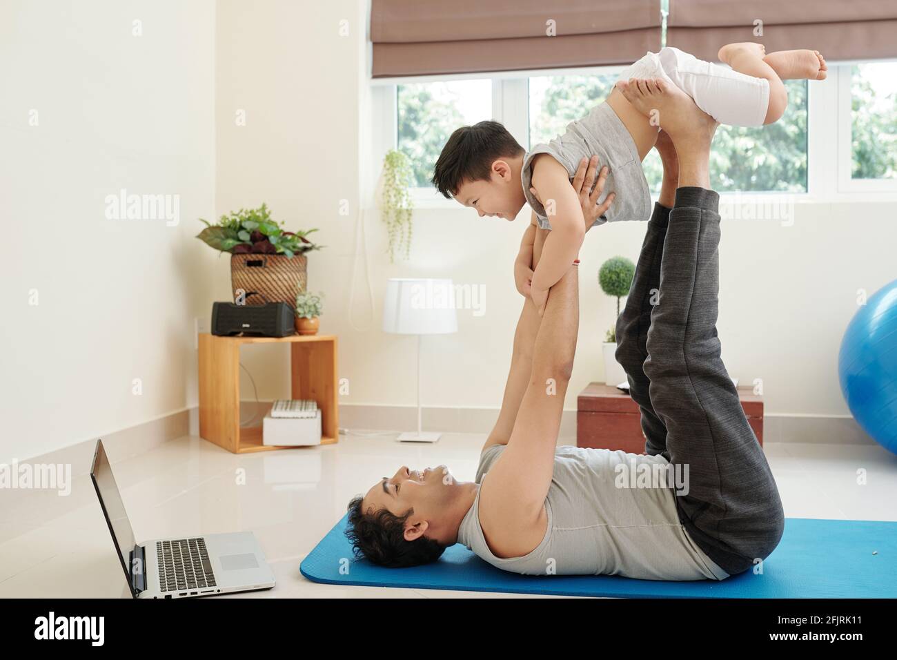 Lächelnder Inder, der auf einer Yogamatte liegt und mit ihm spielt Sein lachender kleiner Sohn Stockfoto