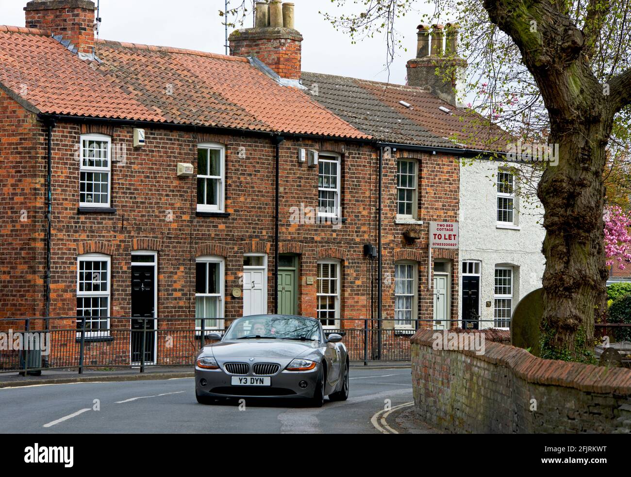 BMW-Sportwagen, der an einer Reihe von gemauerten Reihenhäusern in Cottingham, East Yorkshire, England, vorbeifährt Stockfoto
