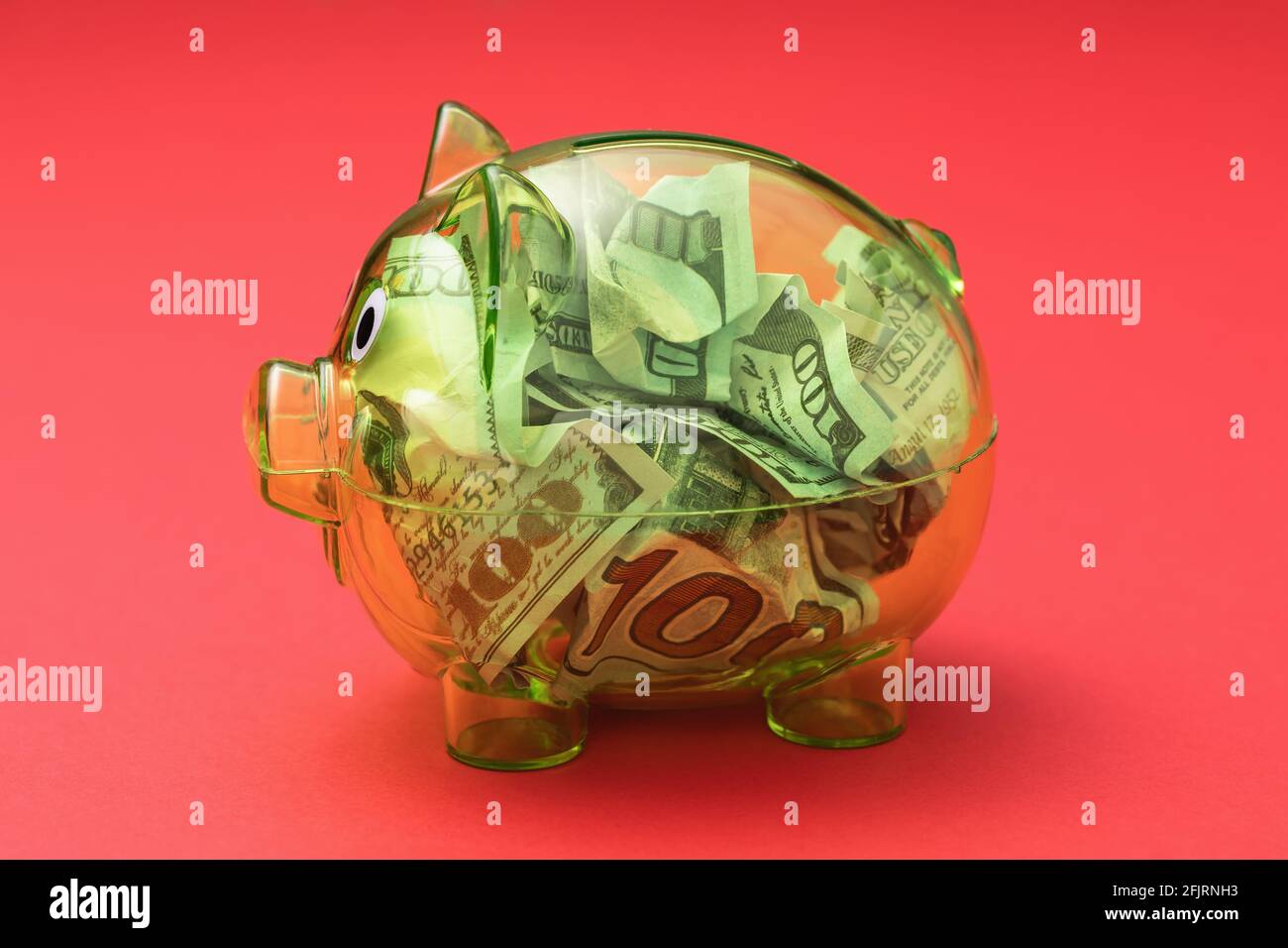 Transparente Sparschwein voller Dollar auf rotem Hintergrund. Stockfoto