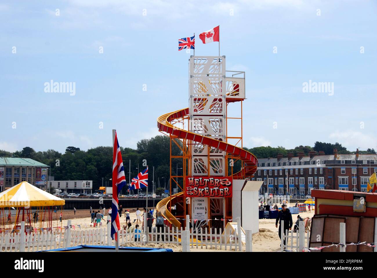 Helter Skelter-Vergnügungsfahrt am Strand, Weymouth, Dorset, England mit Union- und kanadischen Flaggen an der Spitze Stockfoto