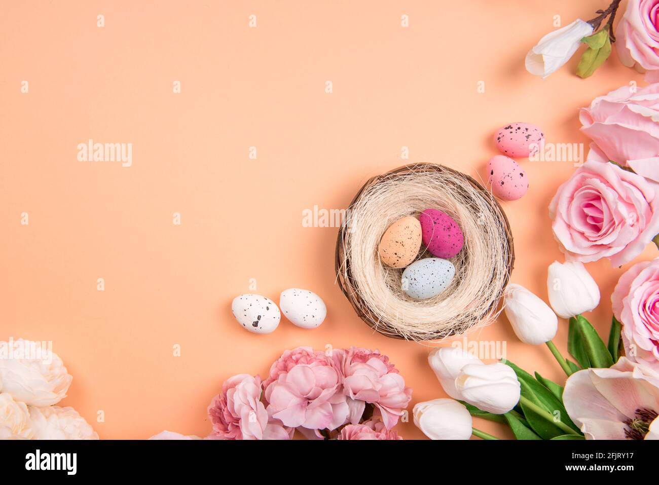 Bunte Dekorationen mit Ostereiernest mit Frühlingsblumen auf orangefarbenem Hintergrund. Copy Space, Draufsicht Stockfoto