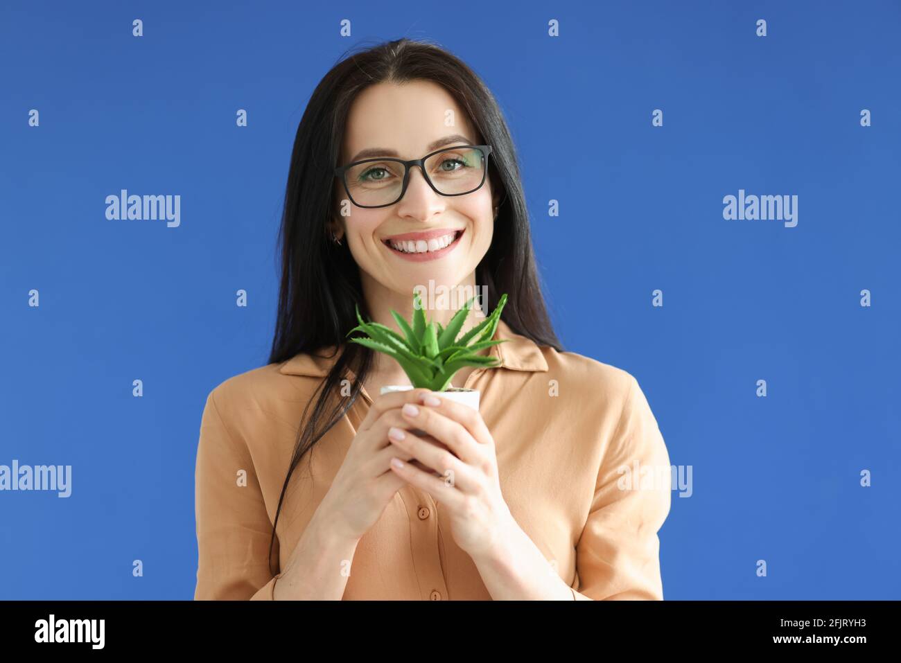 Frau mit Brille, die den Blumentopf in den Händen auf Blau hält Hintergrund Stockfoto