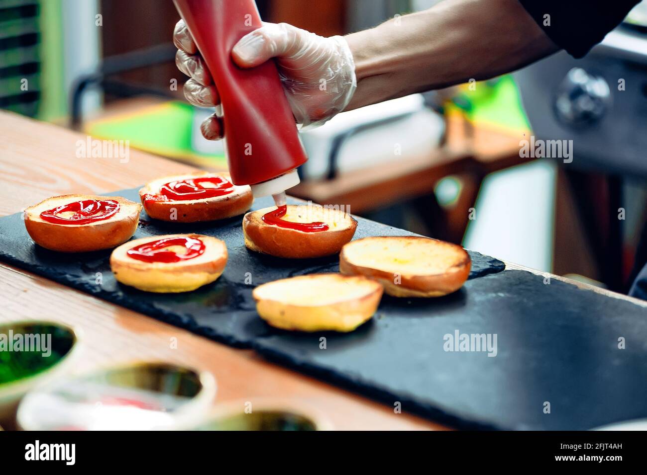 Der Küchenchef verteilt Ketchup auf Hamburgerbrötchen Stockfoto