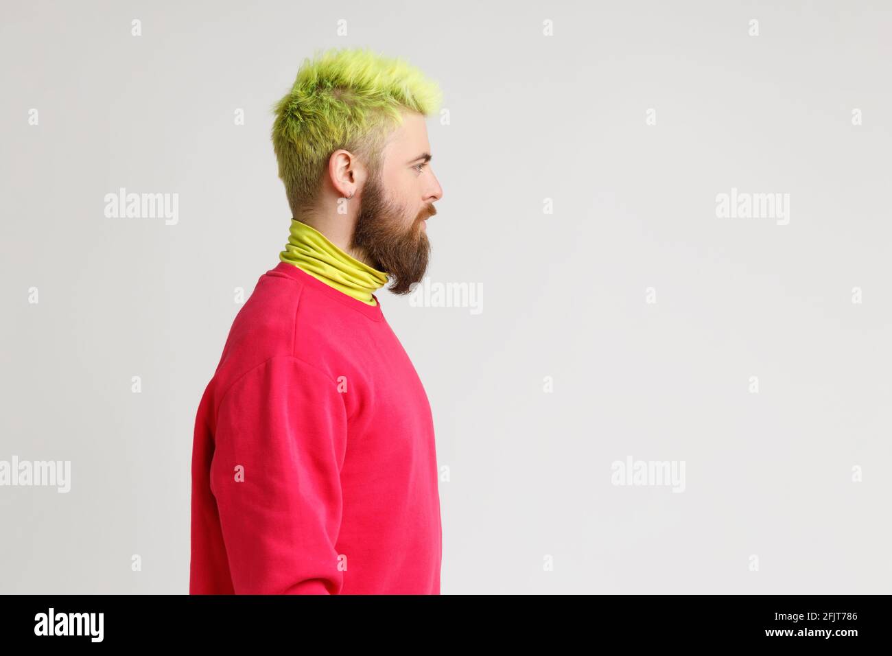 Seitenansicht Porträt eines Mannes mit Bart und gelben Haaren, der mit ernstem und selbstbewusstem Ausdruck vor ihn blickt, einen roten Pullover trägt, Platz zum Kopieren. Indo Stockfoto