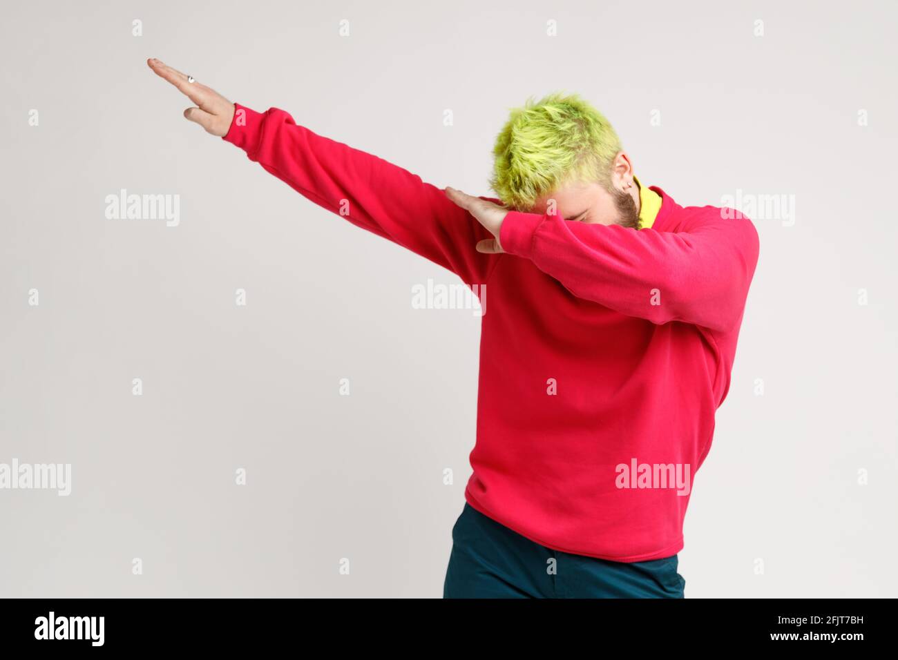 Foto von aufgeregt Mann mit gelben Haaren, zeigt beliebte Internet Meme Pose, feiert Erfolg Sieg, Dabbing Trends, drückt positiv aus. Stu Stockfoto