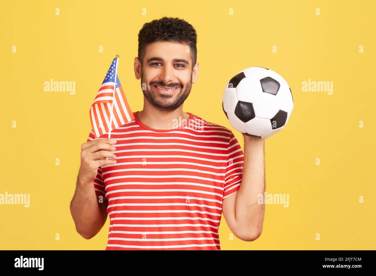 Lächelnder, positiver Mann mit Bart im gestreiften T-Shirt mit der Flagge  der vereinigten Staaten von amerika und der schwarzen und weißen Fußball-Kugel,  united Soccer League. Ind Stockfotografie - Alamy
