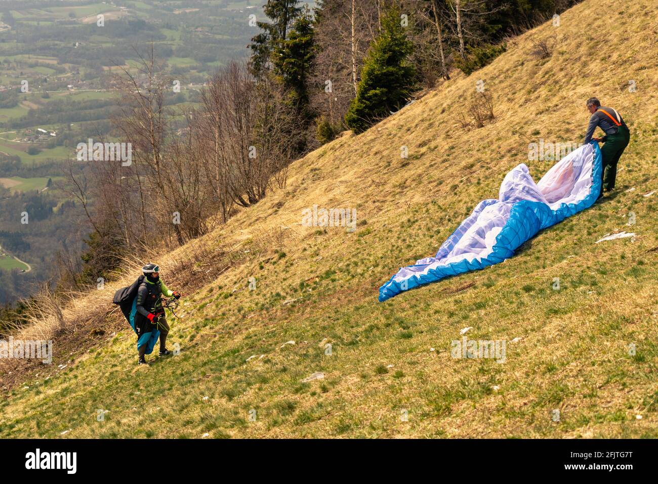 Männer auf einem grasbewachsenen Hang bereiten den Gleitschirm von der ERE Refuge aus vor. San Gregorio nelle Alpi, Belluno, Italien Stockfoto