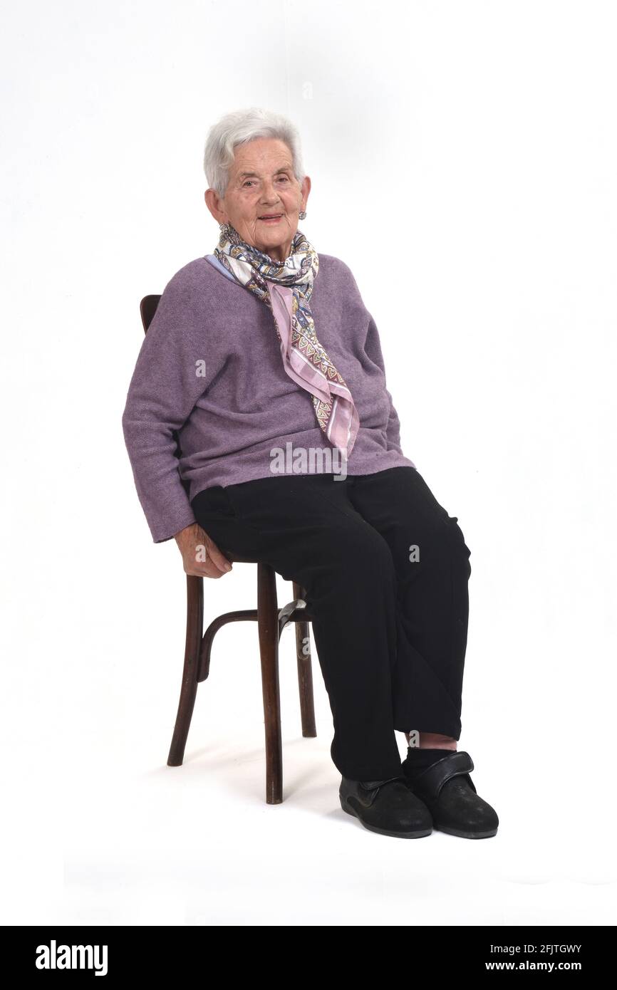 Vorderansicht einer älteren Frau, die auf einem Stuhl sitzt und anschaut Kamera und lächelnd auf weißem Hintergrund Stockfoto