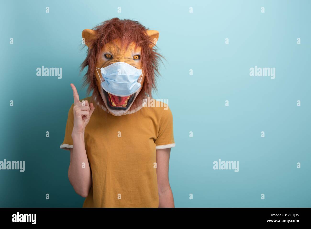 Junge Frau trägt Löwen und Schutz medizinische Maske nach oben mit Zeigefinger, erfassen die Aufmerksamkeit oder Warnung Rat, isoliert auf blauem Hintergrund Stockfoto