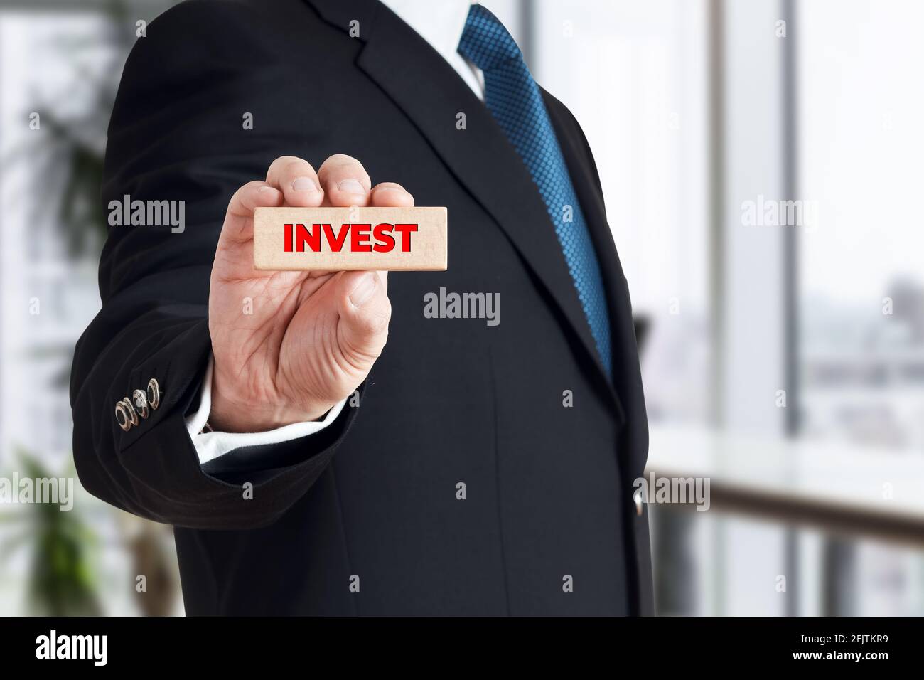 Geschäftsmann zeigt einen Holzblock mit dem Wort Invest. Entscheidungskonzept für finanzielle Investitionen. Stockfoto