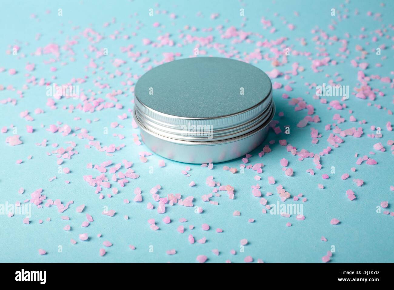 Metallglas mit Creme auf blauem Hintergrund mit rosa Salz. Aluminiumtopf für Naturkosmetik. Aromatherapie. Hautpflege. Creme Stockfoto