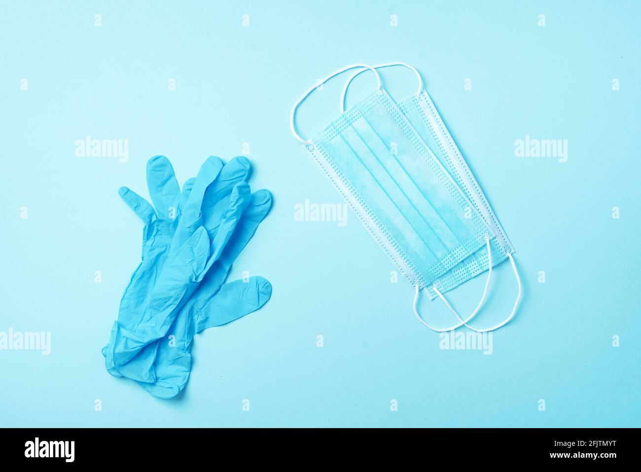Chirurgische Gesichtsmaske und medizinische Handschuhe auf blauem Hintergrund mit Kopierraum. Minimales medizinisches Konzept. Medizinische Geräte. Produkte, die sicher bleiben während Stockfoto
