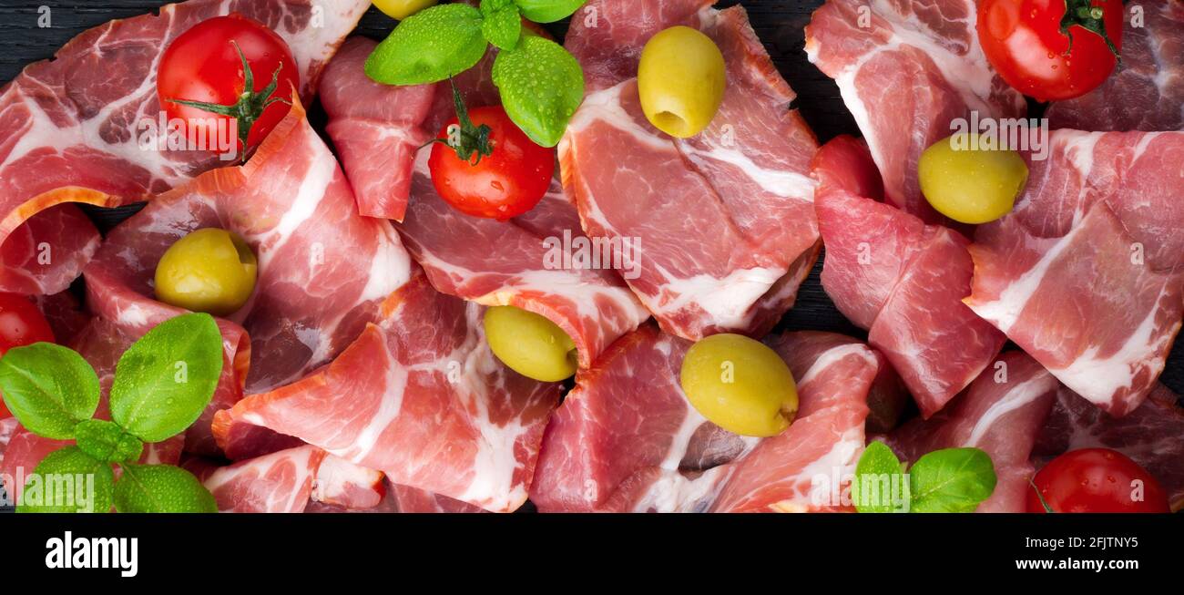 Getrocknetes Fleisch, Jamon mit Kirschtomaten, Basilikum und Oliven auf schwarzem Hintergrund. Selektiver Fokus.Draufsicht. Speicherplatz kopieren. Stockfoto