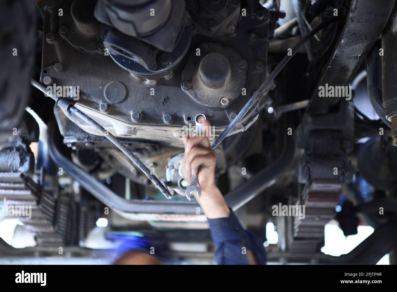 Ein Motormechaniker arbeitet an einem Getriebe unter einem Schwerlastwagen in einer Grube einer Werkstatt mit einem Steckschlüssel. Stockfoto