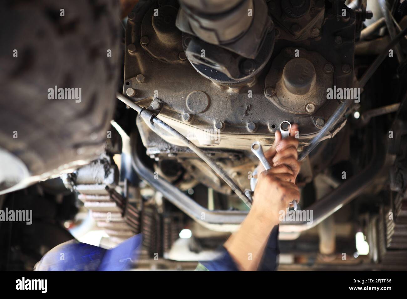Ein Motormechaniker arbeitet an einem Getriebe unter einem Schwerlastwagen in einer Grube einer Werkstatt mit einem Steckschlüssel. Stockfoto