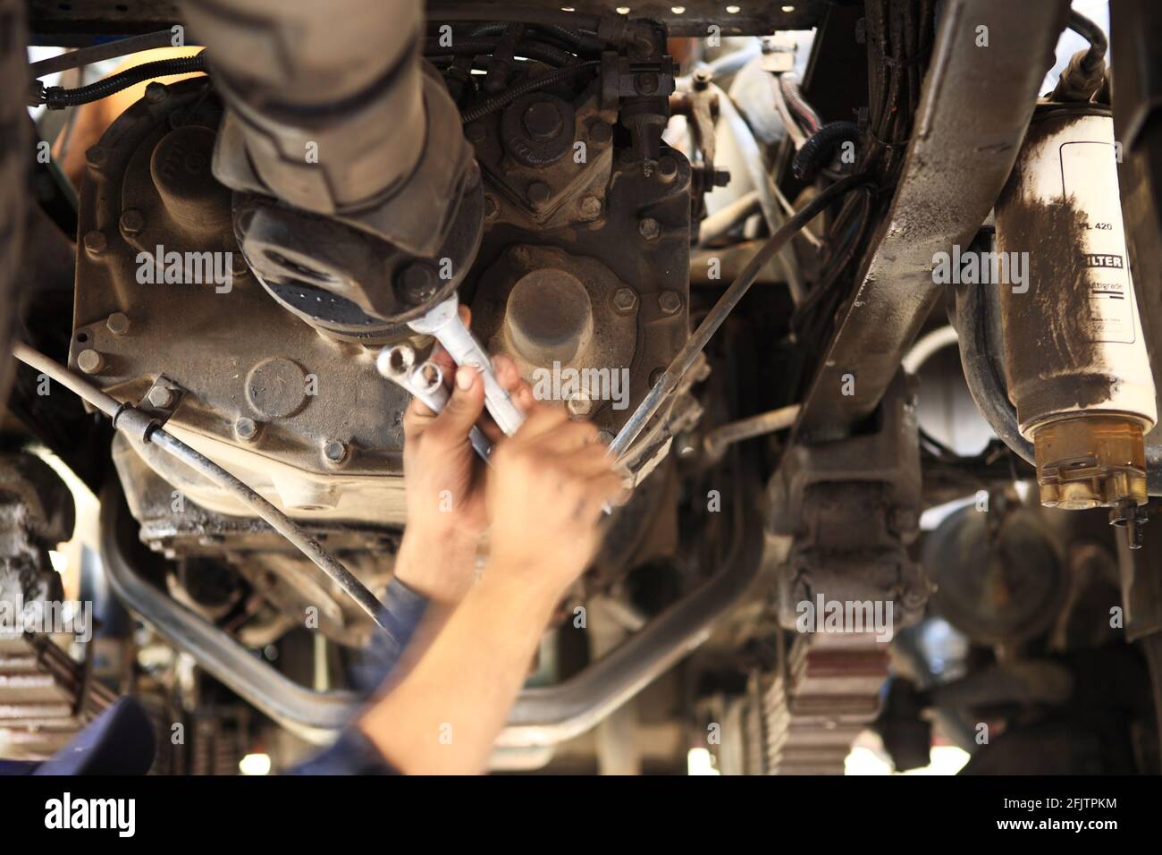 Ein Motormechaniker arbeitet an einem Getriebe unter einem Schwerlastwagen in einer Grube einer Werkstatt mit Doppelschlüssel. Stockfoto