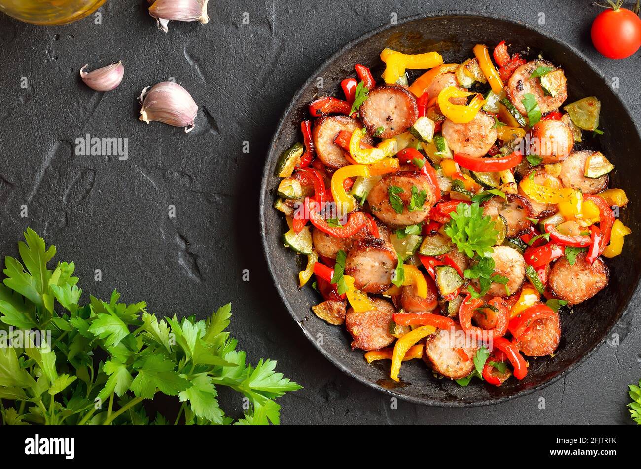 Scheiben von gebratenem Gemüse mit Würstchen und Gewürzen in der Pfanne. Ansicht von oben, flach Stockfoto