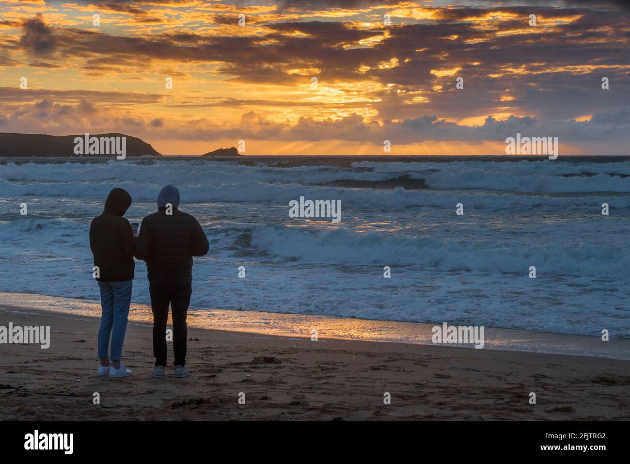 Menschen, die am Fistral Beach stehen und einen spektakulären Sonnenuntergang in Newquay in Cornwall beobachten. Stockfoto
