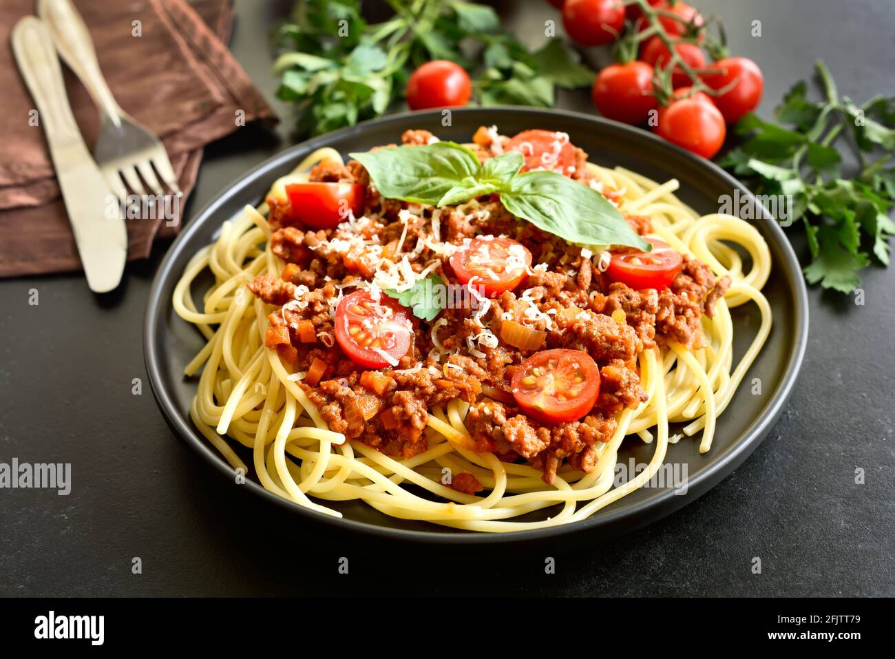 Leckere Spaghetti mit Hackfleisch, Kirschtomaten und Parmesankäse auf schwarzem Stein Stockfoto