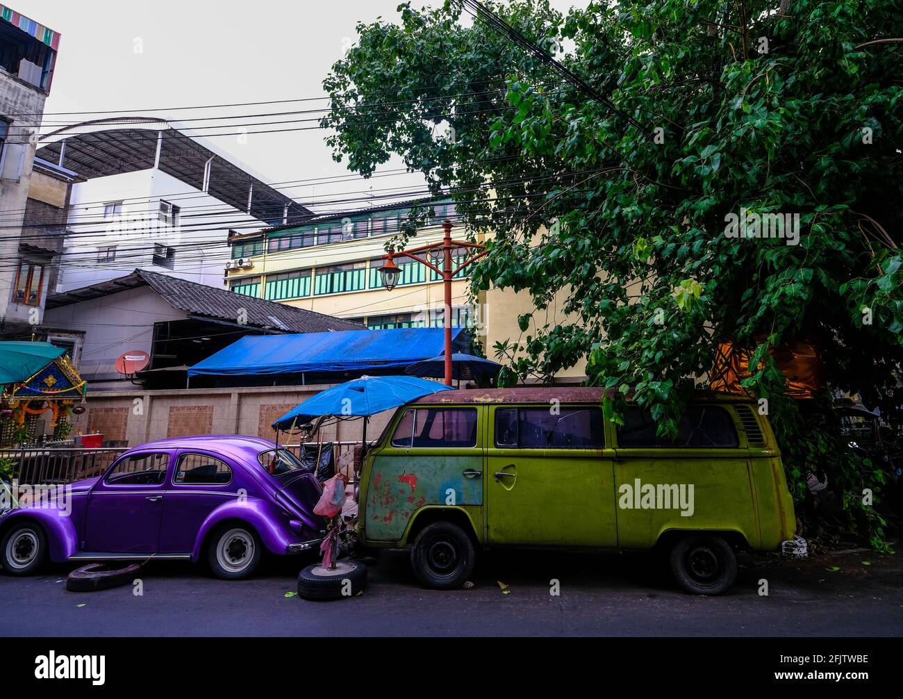 In einer Straße in der Chinatown-Gegend von Bangkok, Thailand, stehen ein alter, lila VW Käfer und ein grüner VW Dormobile Stockfoto