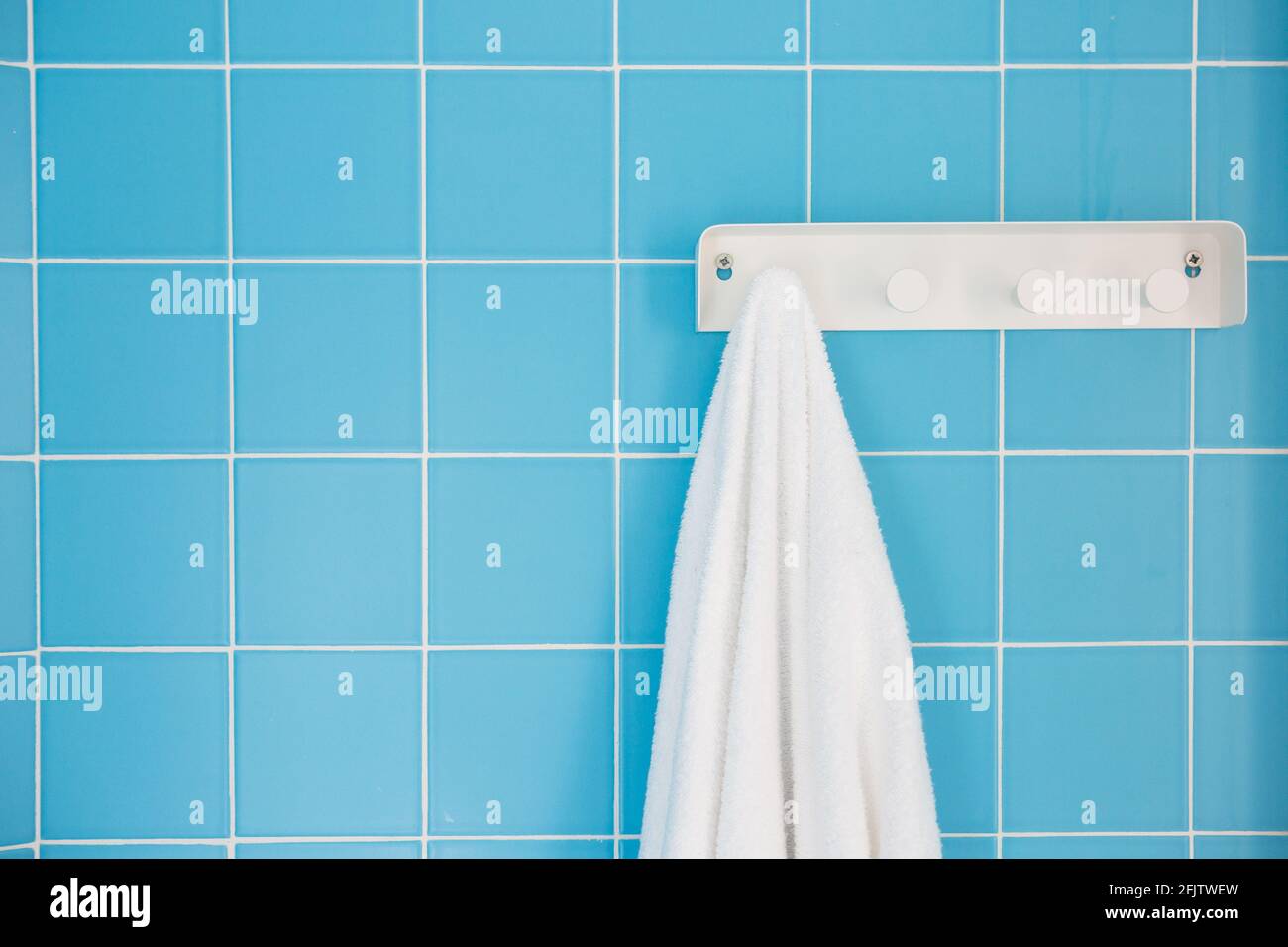 Weißes Handtuch, das an einem weißen Kunststoffhaken an einem hängt Blau geflieste Wand Stockfoto
