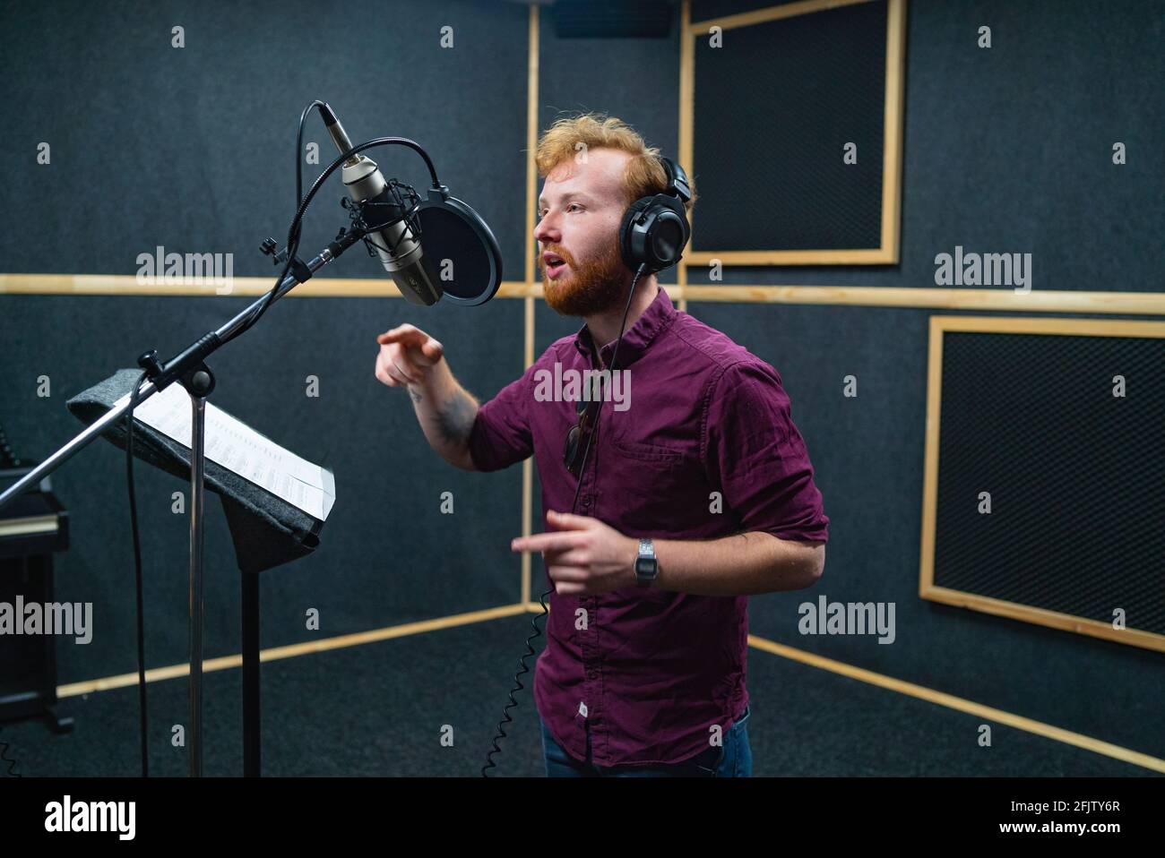 Bärtiger junger Mann bleibt in der Nähe des Mikrofons und nimmt Stimme im professionellen Studio auf Stockfoto