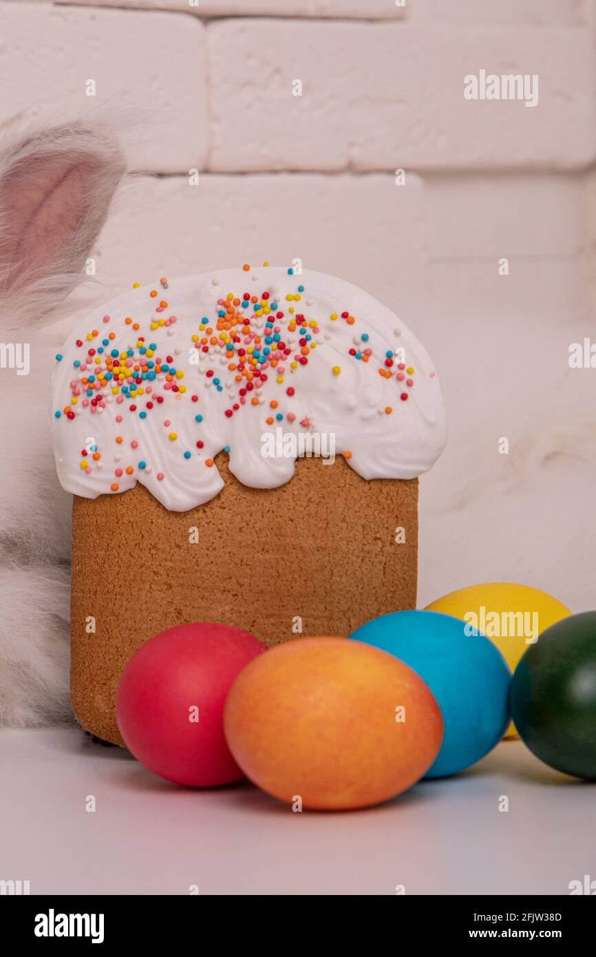 Osterkuchen und bunte Eier in verschiedenen Farben liegen im Vordergrund. Mauerwerk im Hintergrund. Osterhasen-Ohr Stockfoto
